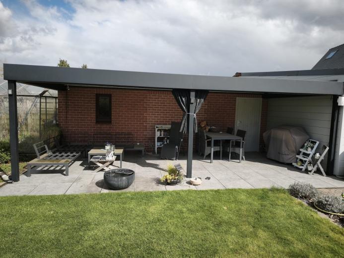 Luxe antraciet aluminium terrasoverkapping aan een bakstenen muur met moderne lounge-set en verlichting.