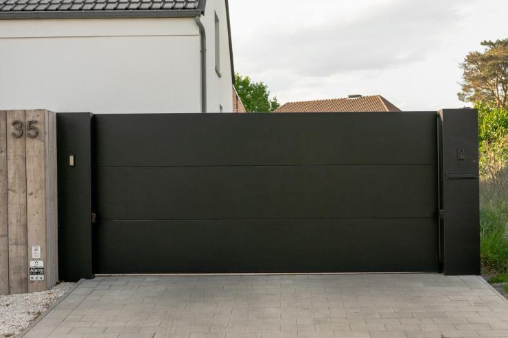 Moderne zwarte schuifpoort met brievenbus bij witte woning