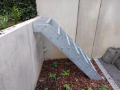 Zijaanzicht van een verzinkte stalen buitentrap met roostertreden gemonteerd tegen een betonnen keerwand.