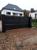 Moderne zwarte aluminium schuifpoort met horizontale lamellen en dichte panelen voor een oprit.