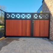 Zwarte metalen draaipoort met verticale houten planken en decoratieve kruisen aan de bovenzijde, gemonteerd naast een bakstenen muur.