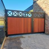 Zwarte metalen draaipoort met verticale houten planken en decoratieve kruisen aan de bovenzijde, gemonteerd naast een bakstenen muur.