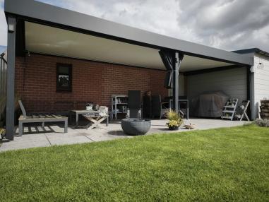 Luxe antraciet aluminium terrasoverkapping aan een bakstenen muur met moderne lounge-set en verlichting.