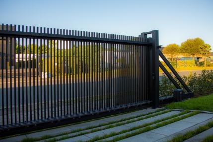 Zwarte vrijdragende schuifpoort met modern spijlenwerk en elektrische motor op een betonnen oprit.