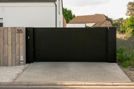 Moderne zwarte schuifpoort met brievenbus bij witte woning